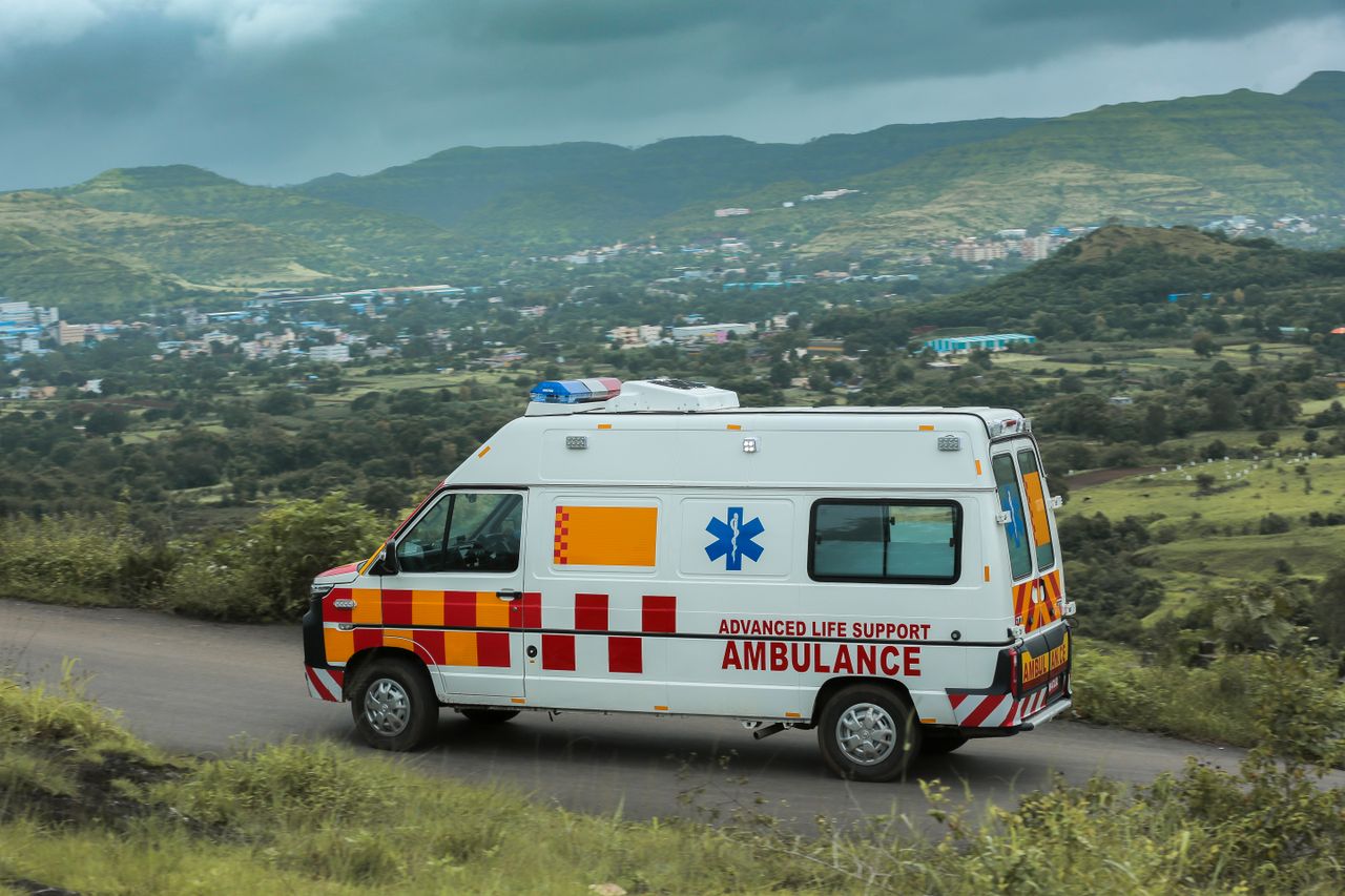 hero-img-02 Advanced life support ambulance driving on a scenic road in Pune, India with lush green hills in the background.